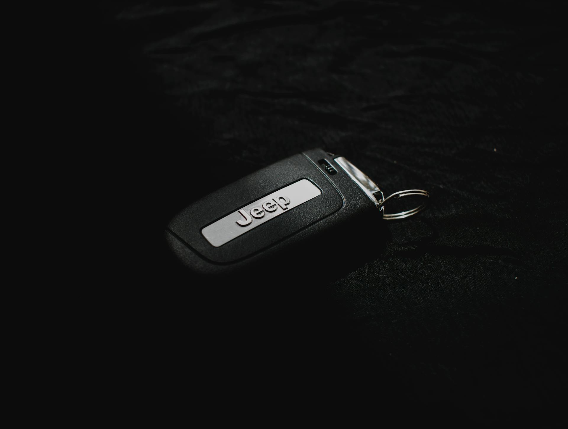 Minimalist close-up of a Jeep car key resting on a dark surface for automotive themes.