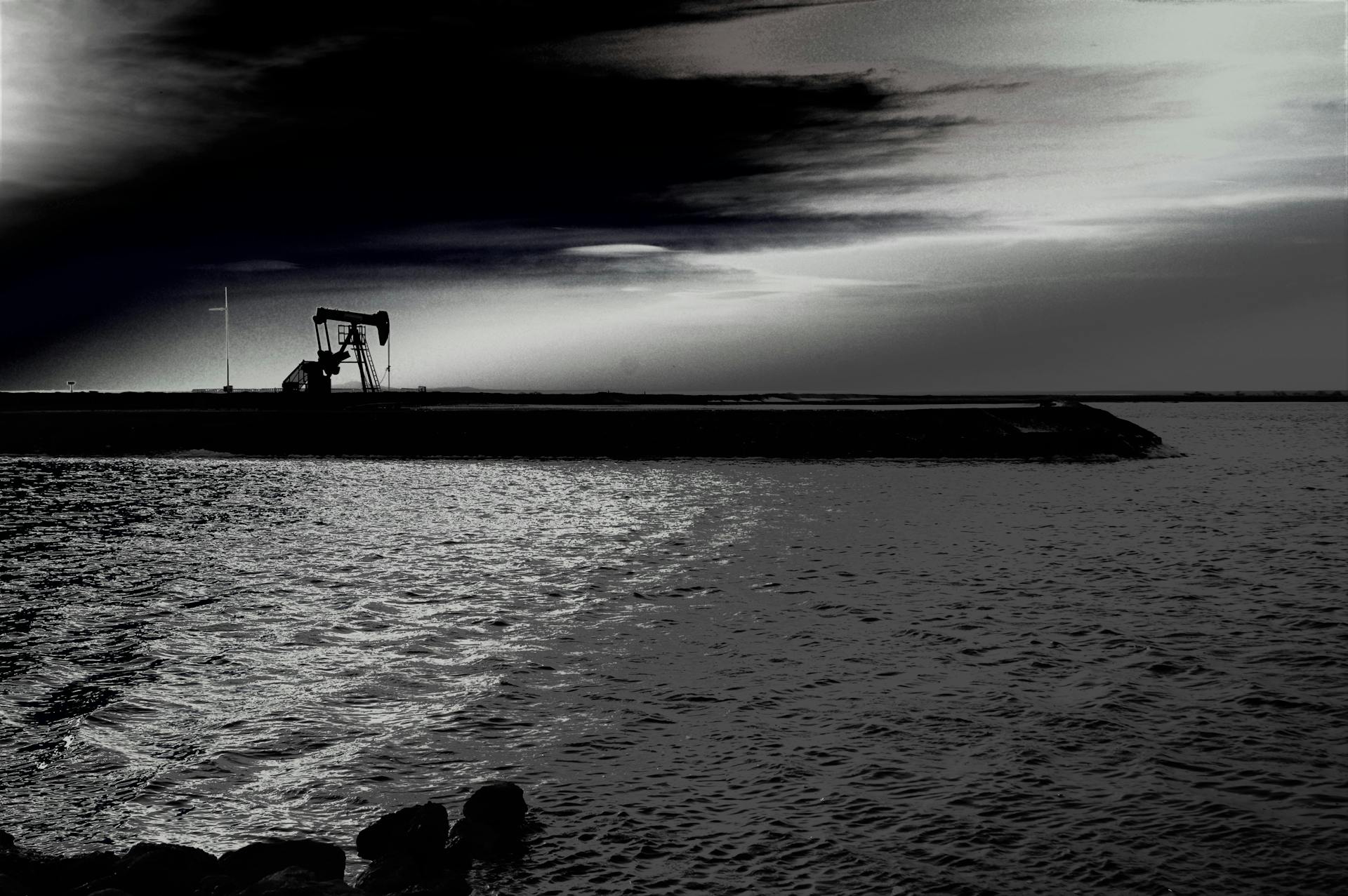 A dramatic silhouette of an oil rig against a stunning sunset over a reflective lake.