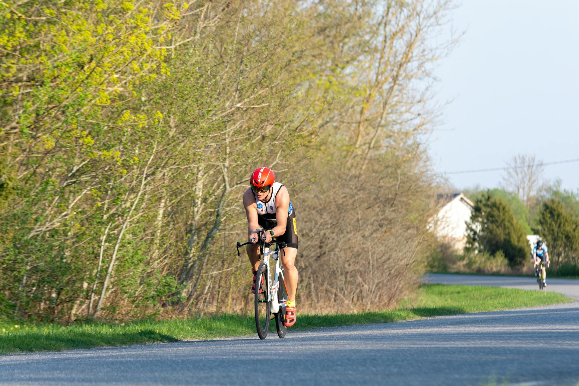 Focused cyclist competing in a triathlon on a scenic rural road with trees lining the path.