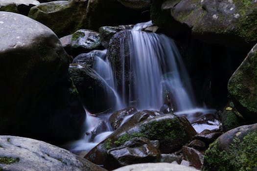Long exposure of a serene waterfall cascading over mossy rocks in a tranquil forest setting.