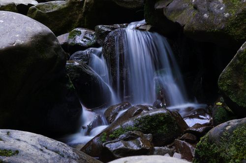 Free Long exposure of a serene waterfall cascading over mossy rocks in a tranquil forest setting. Stock Photo
