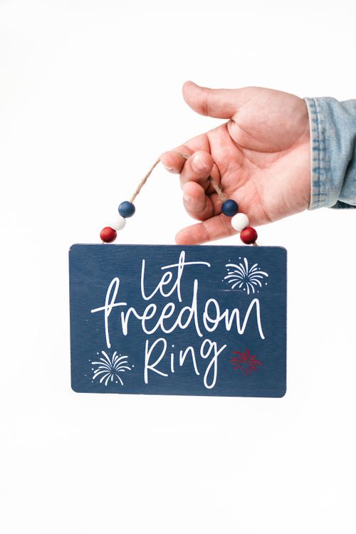 Free Close-up of a hand holding a patriotic sign with fireworks illustration and the phrase "Let Freedom Ring." Stock Photo