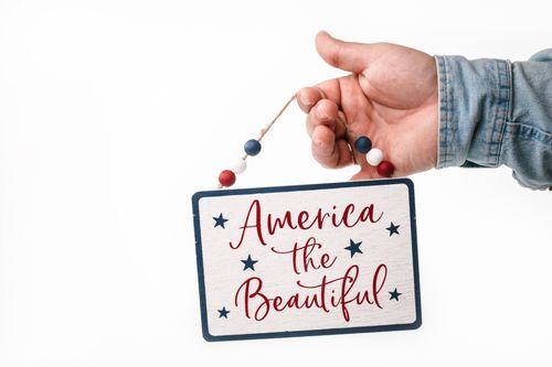 Free Close-up of a hand holding a patriotic sign with 'America the Beautiful' text. Stock Photo