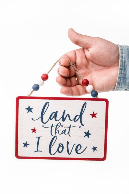 Free Hand holding a patriotic sign saying 'Land That I Love' on a white background. Stock Photo