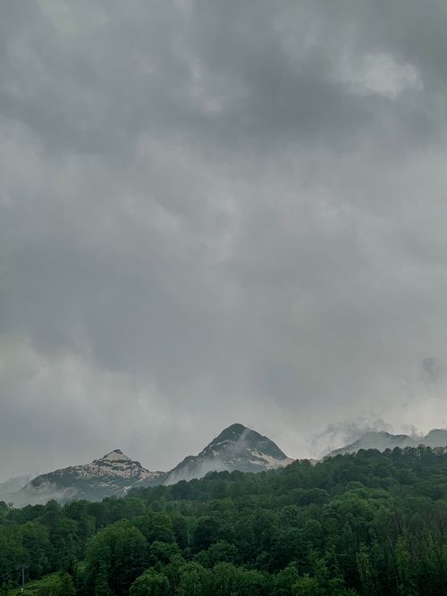 Free Aerial view of mountains under a gloomy sky, surrounded by lush green trees. Stock Photo