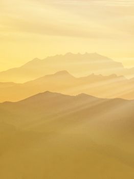 Capture of misty mountain ranges at dawn with warm golden hues and sunlight rays.