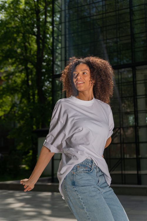 Free Joyful woman with curly hair enjoying a sunny day outdoors in casual attire. Stock Photo