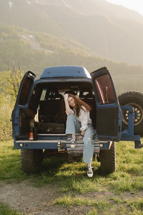 Free Woman sitting in open SUV undermountains. Perfect for travel and lifestyle themes. Stock Photo