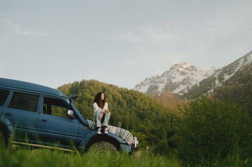 Free A woman sitting on an SUV with scenic mountain views. Perfect for travel and adventure themes. Stock Photo