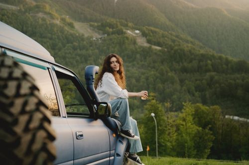 Free Woman sitting on a truck, enjoying a scenic mountain view during sunset. Stock Photo