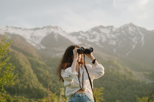 Free A woman uses binoculars to view scenic mountain vistas, embracing adventure and nature. Stock Photo
