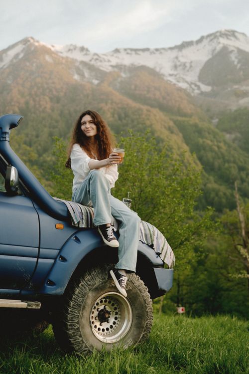 Free Young woman enjoying a serene moment atop a truck in a scenic mountain landscape. Stock Photo
