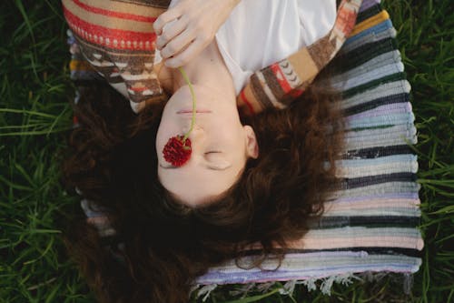 Free A Woman Lying on Green Grass Holding a Flower on her Eyes Stock Photo