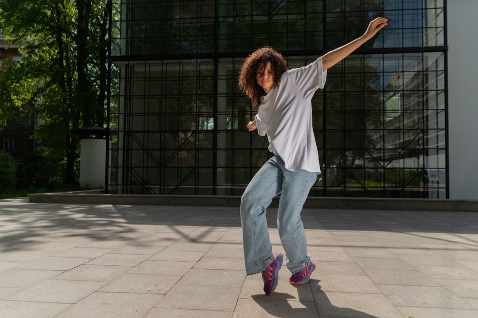 A person dancing outdoors near a modern glass building, enjoying a sunny day.