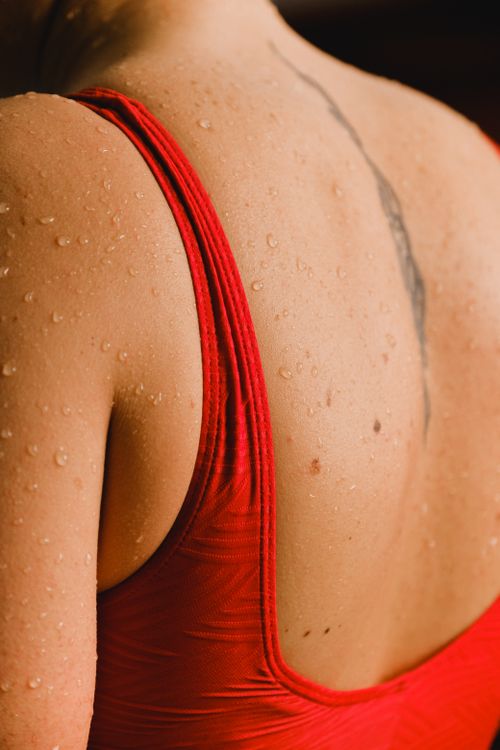 Free Close-up of a woman's back in a red swimsuit with water droplets and tattoo visible. Stock Photo