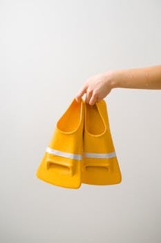 A hand holding a pair of yellow swimming flippers against a white background.