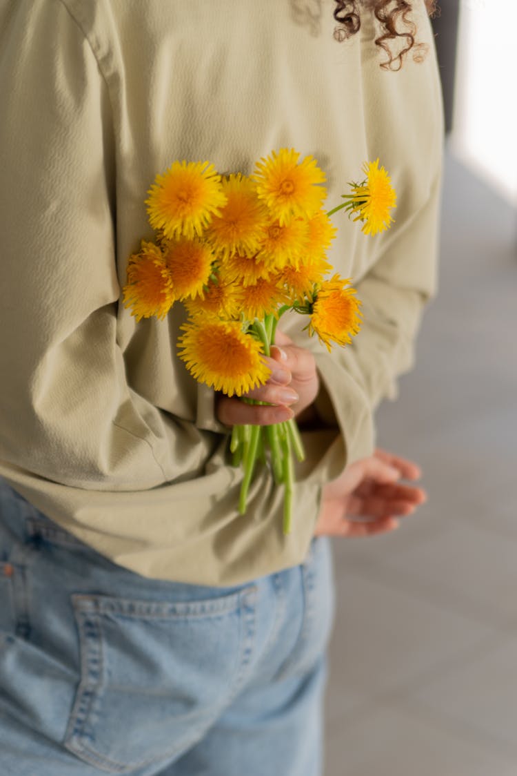 A Person Holding Yellow Flowers At Her Back