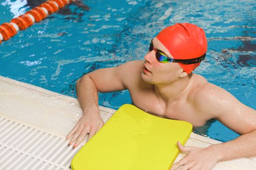 Swimmer wearing a red cap and goggles, resting poolside, exemplifying fitness and water sports.