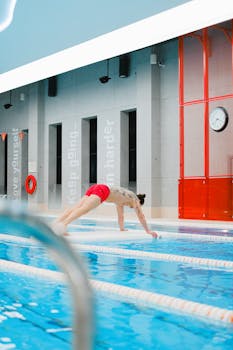 Shirtless man in swimming trunks warms up by an indoor pool, ready for water sports action.