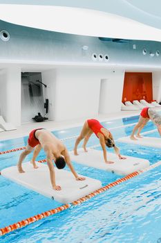 Group performing fitness routines on floating mats in a swimming pool.