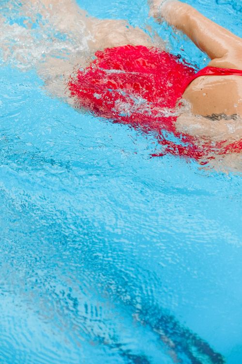 Free Close-up of a swimmer in a red swimsuit making powerful strokes in a bright blue swimming pool. Stock Photo