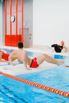 People exercising on floating boards in an indoor swimming pool.