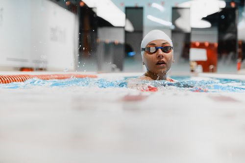 Free A focused female swimmer in an indoor pool, wearing goggles and swim cap, captured in mid-stroke. Stock Photo