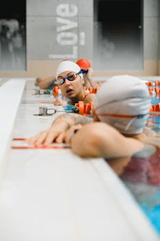 Swimmers in goggles and caps converse at an indoor swimming pool, capturing a dynamic athletic moment.