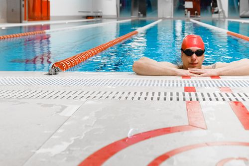 Free Swimmer in red cap and goggles resting by the indoor pool lane divider Stock Photo