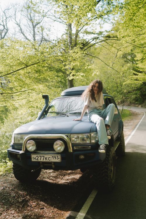 Free Young woman sitting on a blue 4x4 vehicle in a lush green forest, enjoying a peaceful day outdoors. Stock Photo