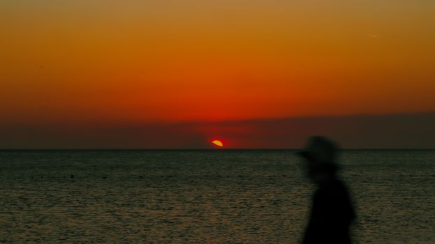 Silhouette of a person by the sea during a vivid orange sunset with a dramatic sky.