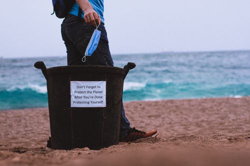 Free A man engages in beach clean-up holding a face mask by the ocean. Stock Photo