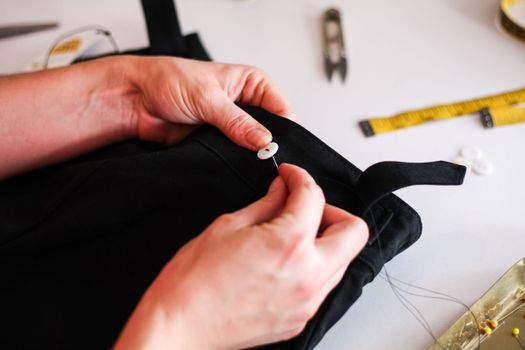 Close-up of hands skillfully sewing a button on black fabric, showcasing attention to detail.