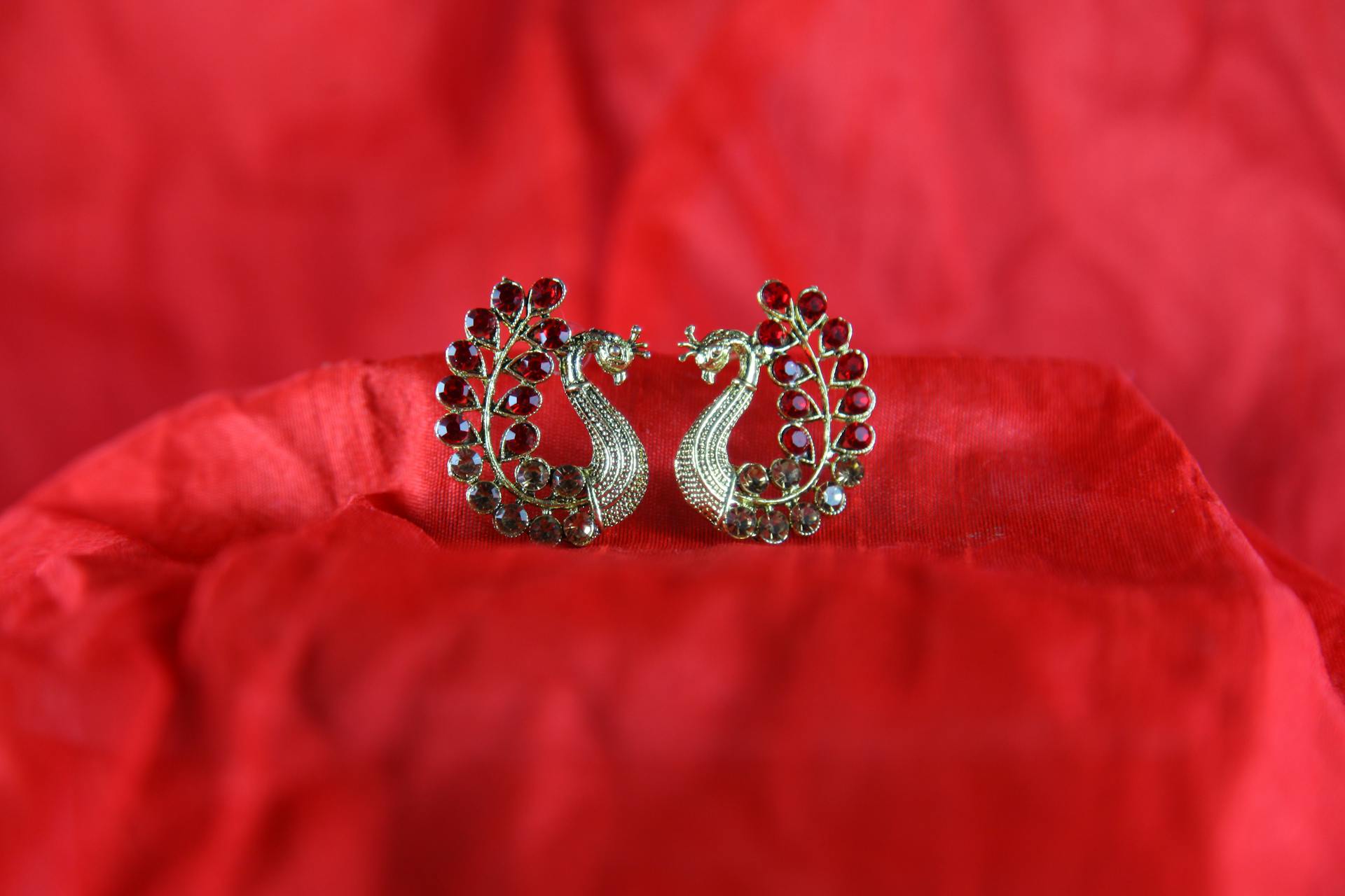 Exquisite gold earrings with red gemstones on rich red fabric, showcasing elegance and traditional Indian design.