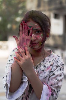 A young Indian woman with color powder on her face celebrates Holi outdoors with joy.