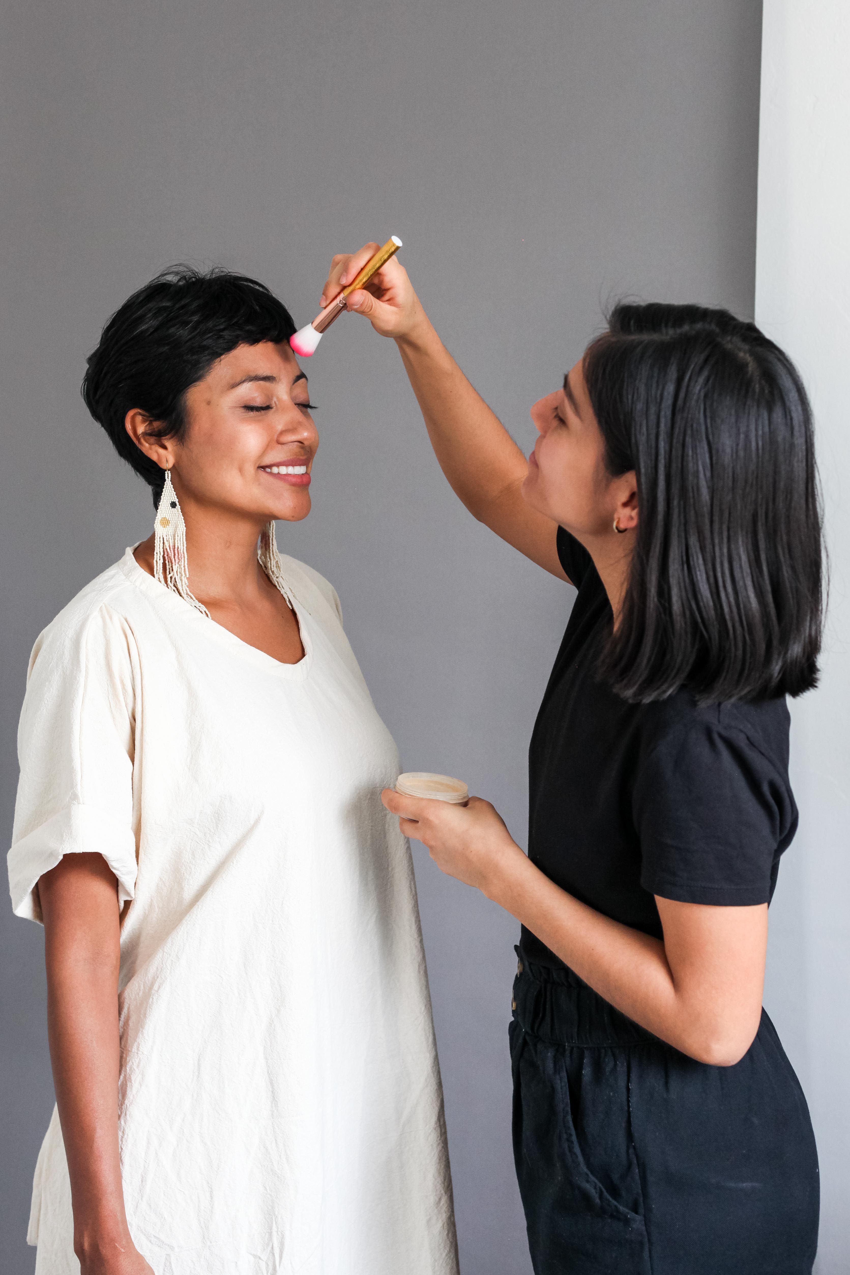 Makeup artist applying cosmetics to a smiling woman indoors.