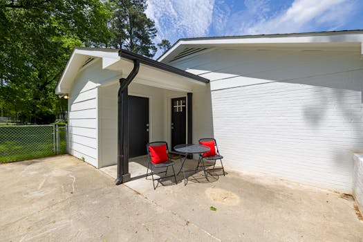 White-bricked home exterior with a small patio setup featuring black chairs and a table.