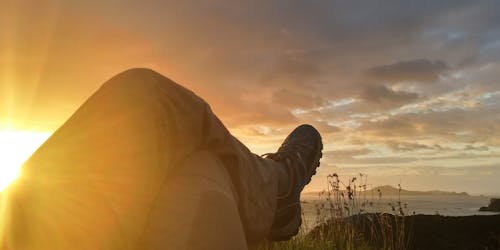 Солнце отражается на скрестив ногу человека под кучевыми облаками во время восхода солнца