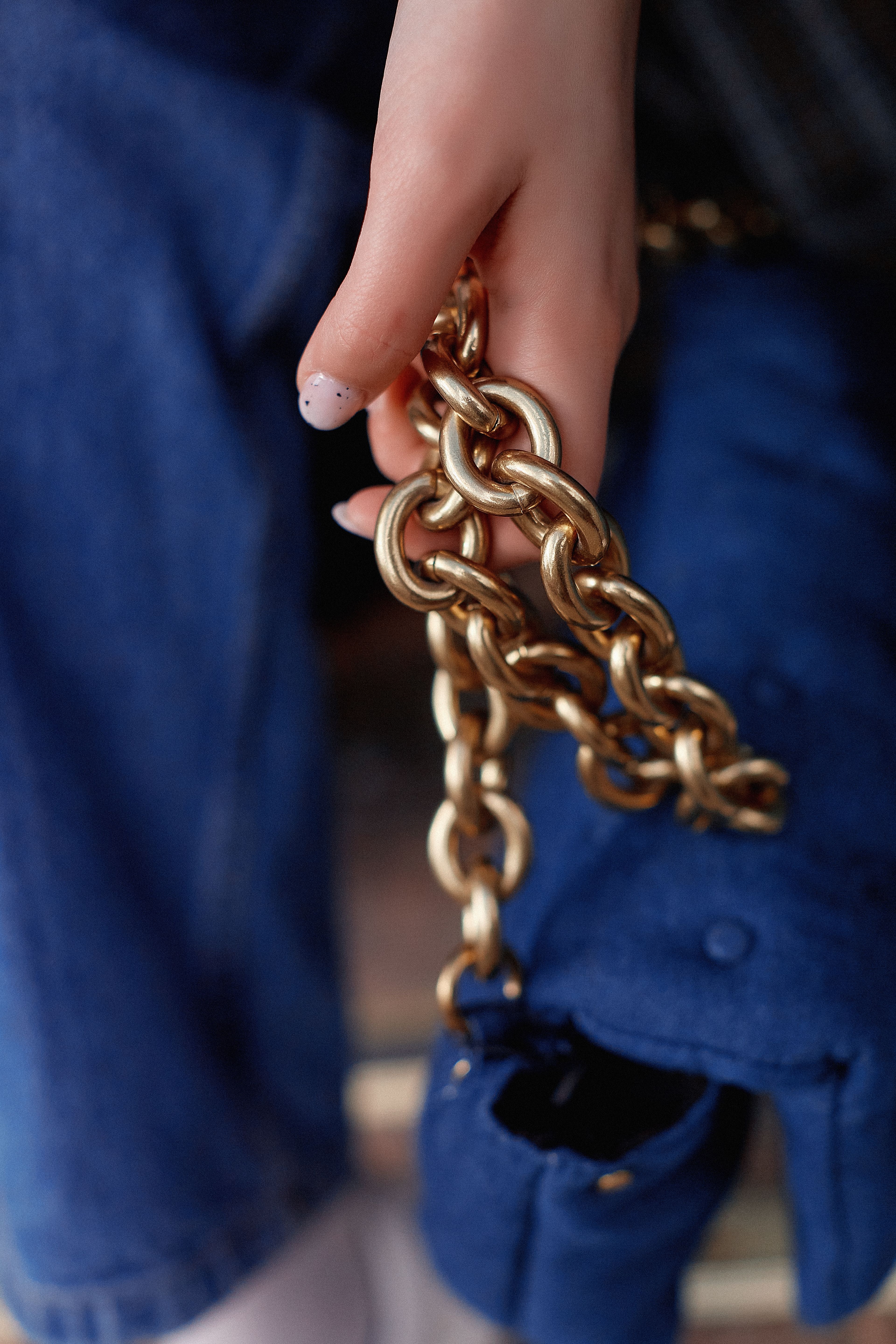 A detailed shot of a hand holding a shiny golden chain against a denim background.