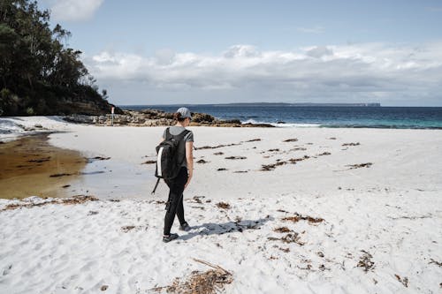 A Person Carrying a Backpack Walking on Shore