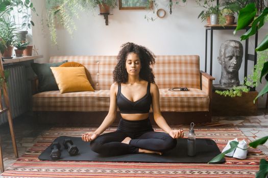 Woman practicing yoga meditation indoors on a mat surrounded by plants, promoting relaxation and wellness.