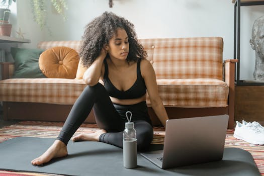 Young woman in activewear practicing yoga at home, using a laptop.