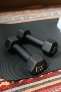 Black 10 lb dumbbells placed on a yoga mat indoors.