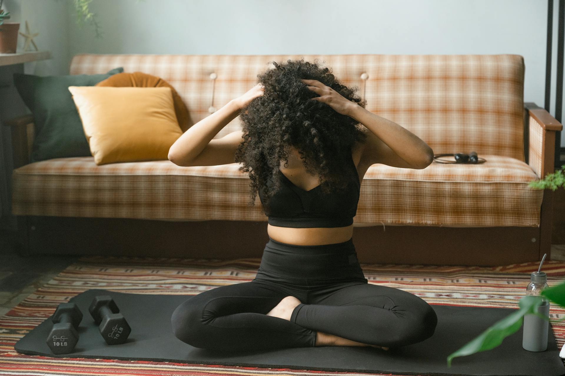 Adult woman performing yoga exercises indoors with dumbbells and yoga mat, fostering health and wellness.