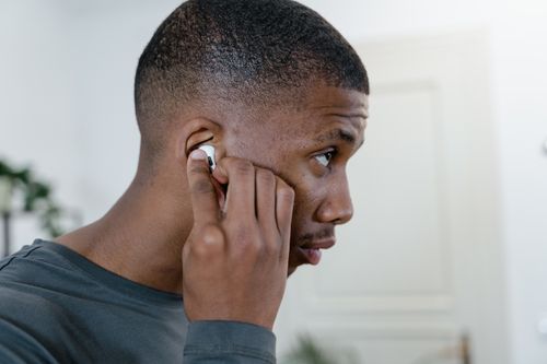 Free Close-up of a man adjusting his wireless earbuds while indoors, showcasing modern lifestyle. Stock Photo