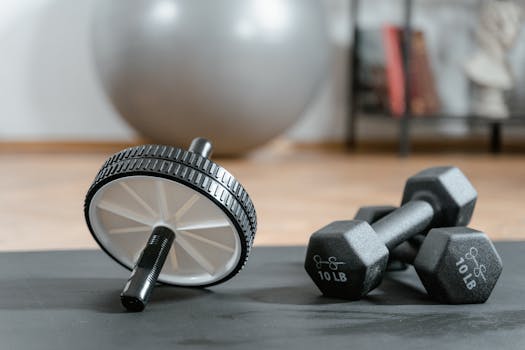 Close-up of ab wheel and dumbbells on a mat in a home gym setting.