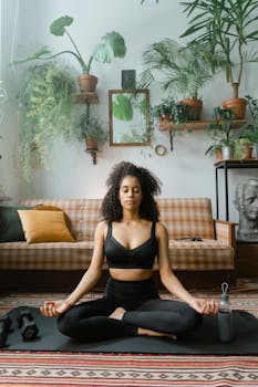 Woman meditating on yoga mat indoors surrounded by plants, embodying calmness.