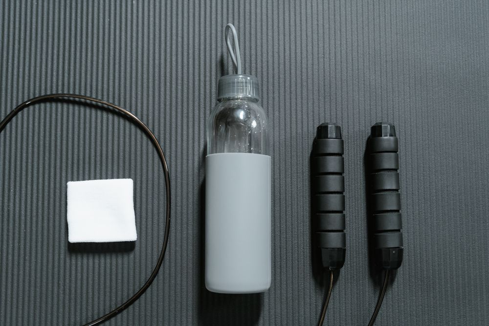 A rolled resistance band, a folded gym towel with a woven label and a laser-engraved steel bottle, arranged on a bench