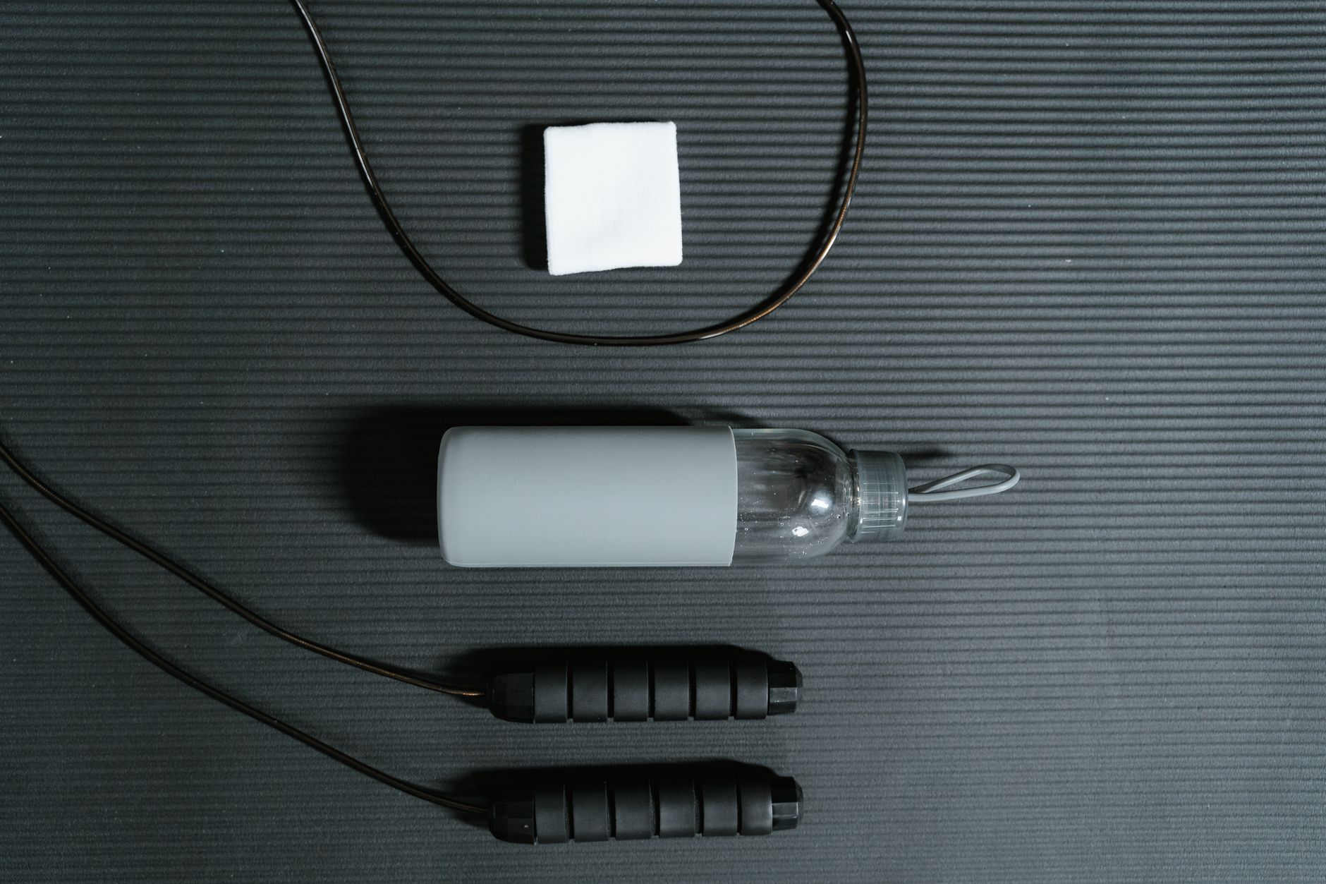 Top view of fitness essentials: jump rope, water bottle, and towel on a mat.