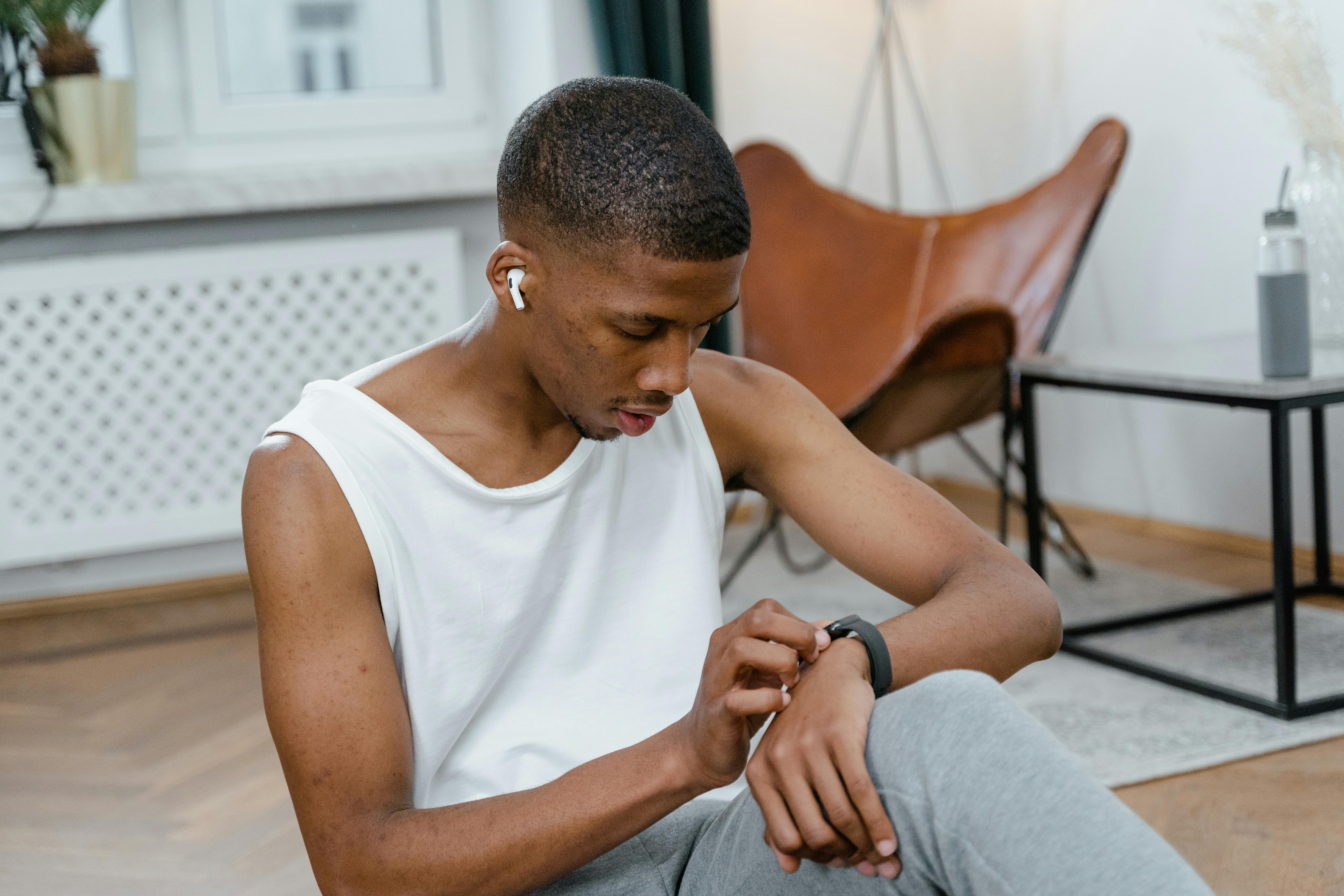 A man indoors uses a smartwatch for monitoring workouts, wearing AirPods.